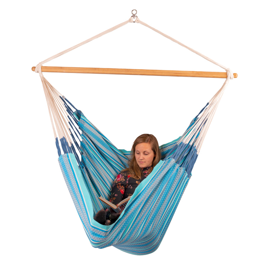 A woman sits in a blue and teal striped fabric hanging hammock with a natural wood spreader bar
