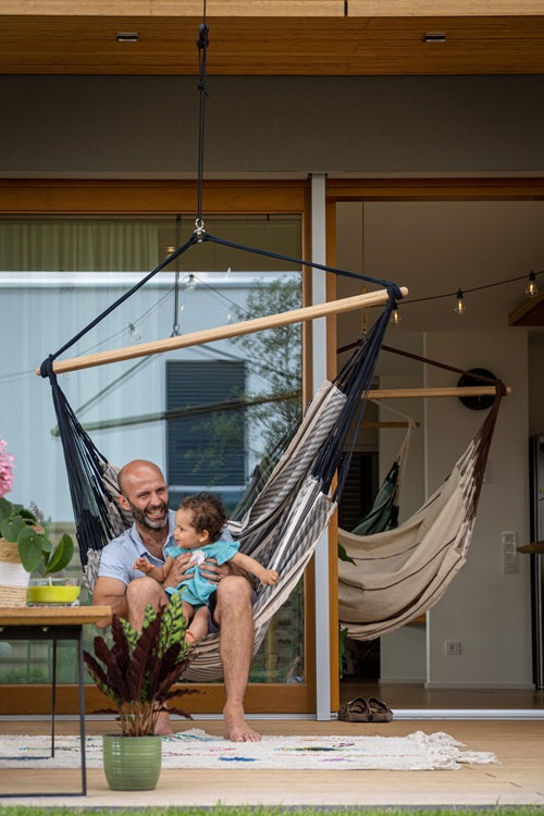 Man sitting in a hammock with a child, surrounded by plants on modern outdoor patio