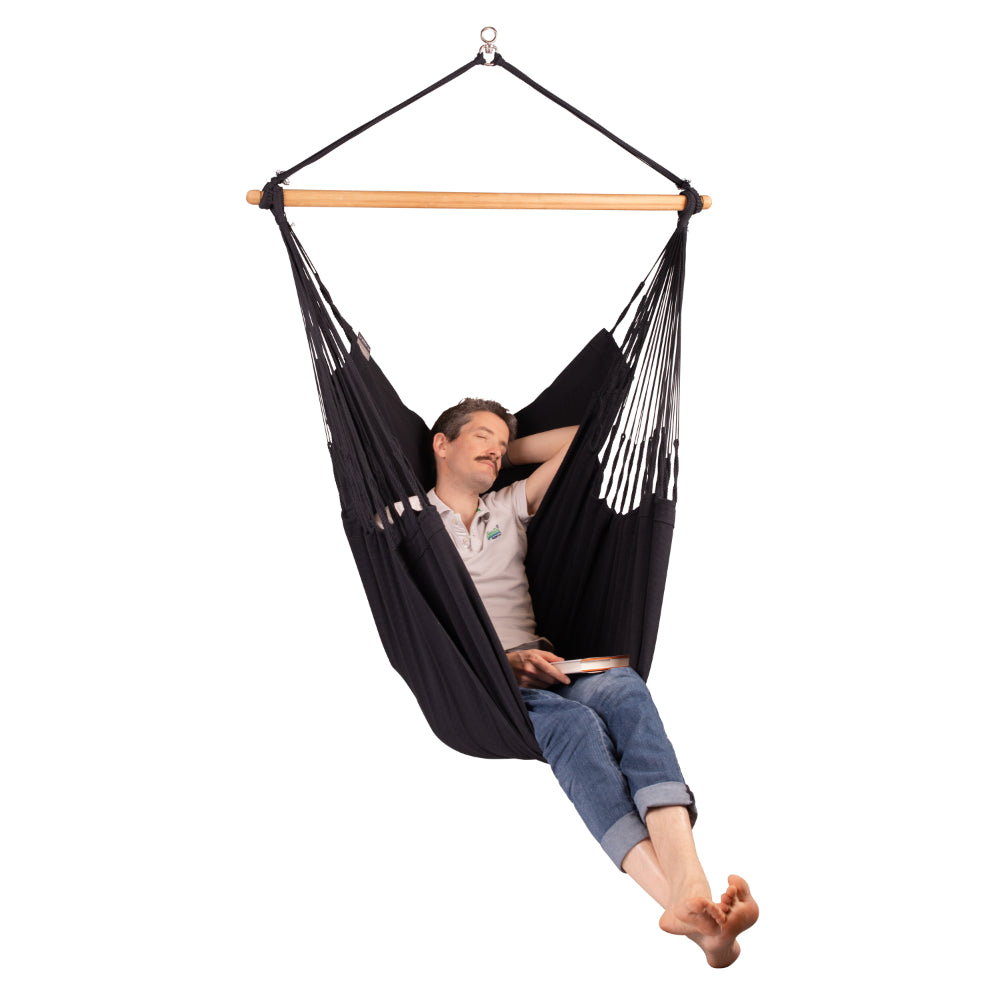 Man holding a book while relaxing in a black hanging hammock chair