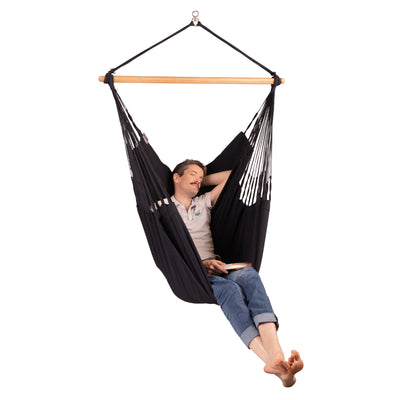 Man holding a book while relaxing in a black hanging hammock chair