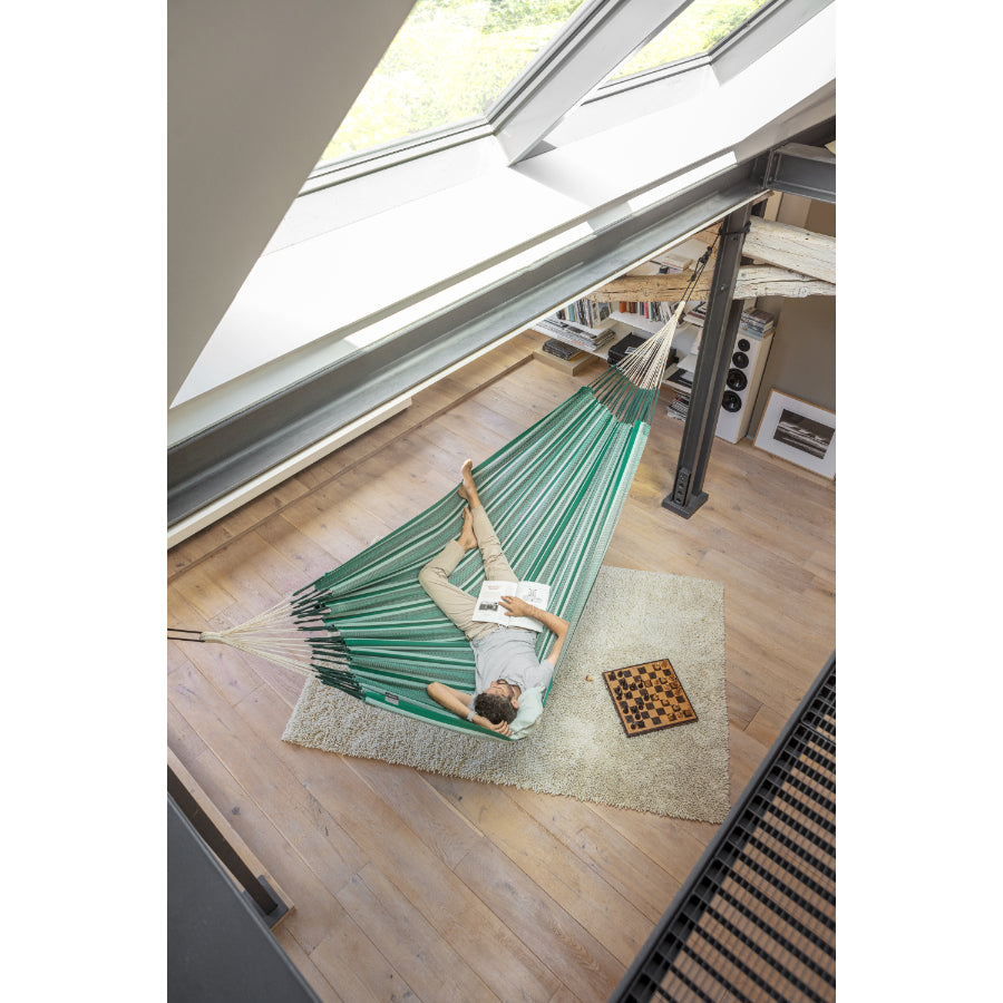 Man napping in large green and white hammock inside