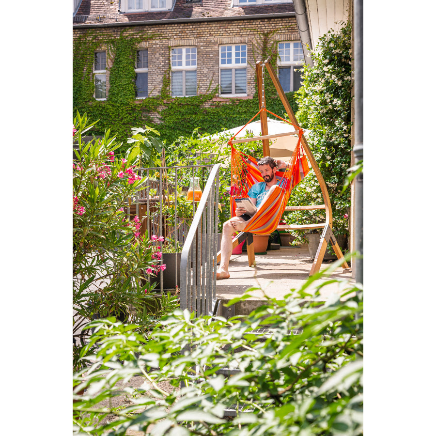 Man reading in colourful hammock chair on garden balcony